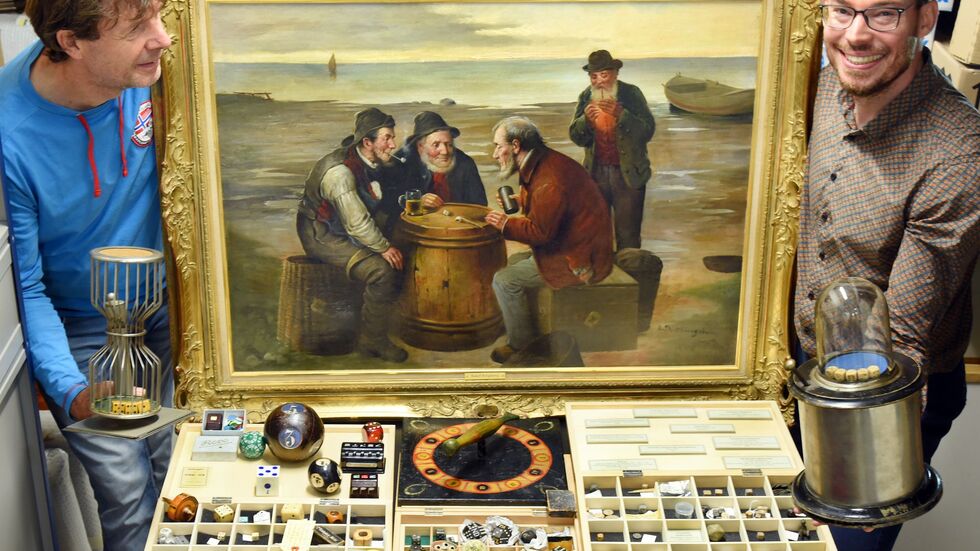 Der Würfelspielesammler Jakob Gloger (r) steht mit seinem Vater Andre Gloger in seiner Würfelspielesammlung, zu der neben vielen Tausenden Würfel auch ein großes Gemälde gehört, das Fischer beim Würfeln auf einem Heringsfass um 1910 zeigt. 