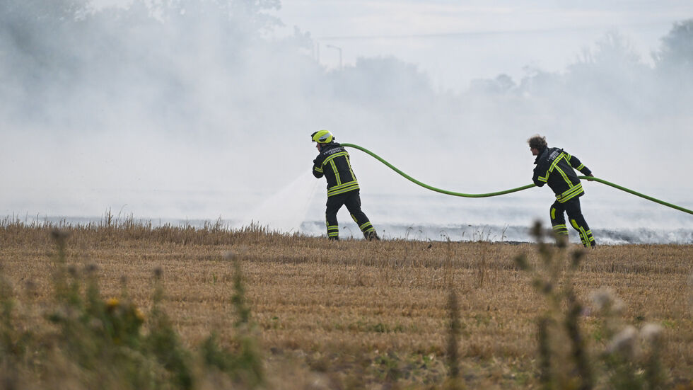 Feuerwehrleute auf dem qualmenden Feld beim Löschen.