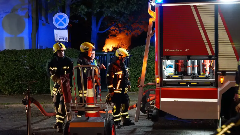 Feuerwehrleute am Brandort, im Hintergrund stehen die Lauben in Flammen.